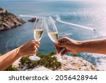 Hands holding champagne glasses over the sea. Romantic vacation. Two hands holding champagne glasses on the background of the sea. A couple in love drinks champagne on the seashore. Copy space