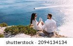Small photo of A couple in love drinking champagne on the seashore, panorama. A happy couple on a honeymoon by the sea, panorama. A beautiful couple with champagne on the coast. Honeymoon. Wedding travel. Copy space