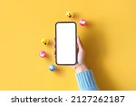 Small photo of Hand of woman holding blank mobile phone with love, like, comment, hashtag button on yellow background. Social media marketing concept