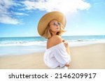 Portrait of blonde caucasian girl in summer straw hat and fashionable sunglasses walking, relaxing at the beach. Vacation vibe. Sunny day. Travel, tourism concept. A lot of copy space.