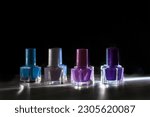 Bottles with pink, purple and blue nail polishes, on a dark background with harsh light and reflections. Low key photo. Beauty and fashion concept. 