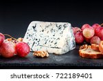 A closeup of a piece of blue cheese with vibrant grapes, slices of bread, and nuts, side view on black textures with a place for text