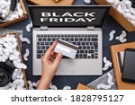 Black Friday concept. Female hand holding a credit card and shopping online through laptop. Computer is surrounded by cardboard boxes with protective foam pads and electronic products inside. Flat lay