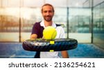 Small photo of Monitor of padel holding black racket with yellow tennis ball over. Class to student on outdoor tennis court. Man paddel player playing a match in the open