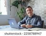 Small photo of Good-looking millennial office employee in glasses sitting at desk in front of laptop smiling looking at camera. Successful worker, career advance and opportunity, owner of prosperous business concept