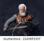 Portrait of gray haired medieval knight with long beard dressed in chain mail holding sword and shield.