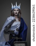 Small photo of Shot of warlike ice queen with sword and shield dressed in cloak and crown.