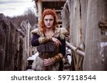 Viking woman with hammer in a traditional warrior clothes. Against the backdrop of a large viking village.