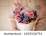 Small photo of Girl holding a spring box of tender pink and violet flowers decorated with green leaves