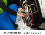 Close-up of man's hands putting on chains on the car wheel on the icy road at winter mountains