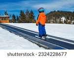 Little boy on the ski moving walkway belt at skiing school during winter vacations view from behind