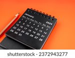 Small photo of January 2024 desk calendar with pencil on orange color background.