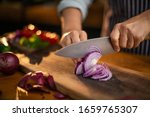 Female chef is precisely slicing red onions on a wooden cutting board in a restaurant. 
