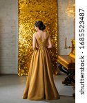 Small photo of Young retro beautiful woman. turned away stands backdrop sparkling golden room, piano. Brunette back finger wave hairstyle. classic elegant evening dress vogue fashion style 1920. Christmas ball