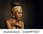 Portrait Closeup Beauty fantasy african woman, face in gold paint. Golden shiny black skin. Fashion model girl mixed race. Glamorous arab turban, jewellery accessories. Professional metallic makeup.