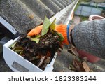 Small photo of A man is cleaning a clogged roof gutter from dirt, debris and fallen leaves to prevent water damage and let rainwater drain properly.