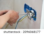 Small photo of New electrical socket installation. An electrician is attaching a new power outlet with power wires to the electrical box, screwing the outlet receptacle, power socket in place.