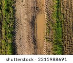 Aerial view of a dirty dirt road with mud, grass and tracks between fields and fields in autumn