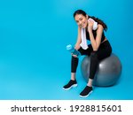 Asian beautiful happy woman holding water bottle and sitting on fit ball after exercise isolated on blue colour background.Concept of slim and healthy girl workout.