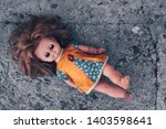 Small photo of Old dirty doll with her eyes closed on concrete floor. The concept of a bygone childhood, loneliness and abandoned