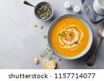 Pumpkin and carrot soup with cream on grey stone background. Copy space. Top view.
