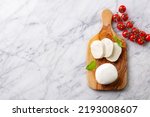 Fresh mozzarella cheese with cherry tomatoes on cutting board. Marble background. Copy space. Top view.