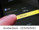 A cryptocurrency investor about to stake Ethereum on a crypto exchange mobile phone app to earn high interest rate. ETH hodler pressing a button to start earning cryptos by staking his holdings.