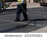 Small photo of Worker spraying slurry tar on street during resurfacing project