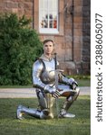 Small photo of Make fealty. Portrait of serious manm medieval warrior, knight in armor sitting on one knee. Knight's noble oath. Comparison of eras, history, renaissance style