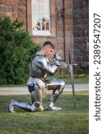 Small photo of Make fealty. Portrait of serious manm medieval warrior, knight in armor sitting on one knee. Knight's noble oath. Comparison of eras, history, renaissance style