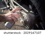 Man's hand using spray can to clean and protect motorbike chain. Concept of maintenance and lubrication of the motorcycle chain.