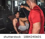 Small photo of A young asian teen does some leg presses while a personal trainer spots to eke some extra reps.