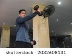 Small photo of A fit man in a sweatshirt does alternating underhand front raises at an open air gym. Strict isolation shoulder workout for front delts.