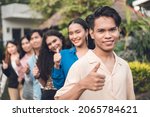 Small photo of A group of six young and dynamic friends from late teens to early 20s, in a single file giving a thumbs up. Outdoor scene.