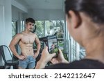 Small photo of A woman taking a picture of a fitness influencer flaunting his impressive physique with her camera, to be posted on social media. A scene at the gym.
