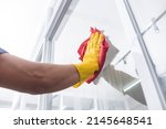 A man wearing yellow gloves wipes clean the surface of a glass window with a red microfiber cloth.