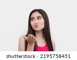 Small photo of An attractive young lady halfheartedly blows a kiss while looking away. Forced, coerced or uninterested action.