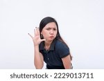 Small photo of A young woman in disbelief and doubt while listening in to some wild and unsubstantiated rumors. Bending to the left, hands on her ear. Isolated on a white background.
