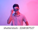 Small photo of A cool asian man puts down his sunglasses to show his steely confident eyes. Lit with blue and pink neon colors.
