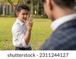 Small photo of An egotistical and cocky young asian man taunts his workmate with a mocking hand gesture. Rivals or enemies in the workplace.