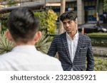 Small photo of A young indian man listens to a colleague while outside the office. A bit annoyed at his cocky workmates smart aleckness and tall tales.