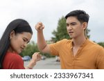 Small photo of A hotheaded and angry young asian man curses and swears at his girlfriend while at the parking lot. An emotionally abusive boyfriend.