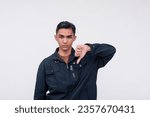 Small photo of A unsympathetic young Filipino man turning down an offer, giving the thumbs down. Isolated on a white background.
