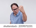 Small photo of A middle aged asian man threatens to hit someone with his fist if they come closer. A hotheaded dad with confrontational behavior. Isolated on a white backdrop.