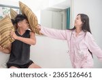 A young asian couple pillow fighting, having fun at the bedroom. A lighthearted moment in the room.
