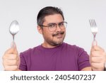 Small photo of A hungry middle aged man holding a spoon and fork looking forward with gusto to a feast. Restaurant and other food advertisement concepts. Isolated on a white background.