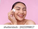 Small photo of A young Asian woman feeling refreshed after using a cotton ball to apply toner or astringent on her forehead. Isolated on a pink background.