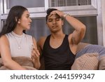 Small photo of A young asian couple in their early twenties faces an unplanned pregnancy, with the man showing stress while sitting on their living room sofa.
