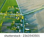 Aerial view over a small village near a dirt road. Large multi-colored fields planted with various agricultural crops. Wheat field from a bird's-eye view.