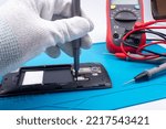 Small photo of Mobile phone repair. The service technician disassembles the phone on the esd mat with a screwdriver, multimeter in the background